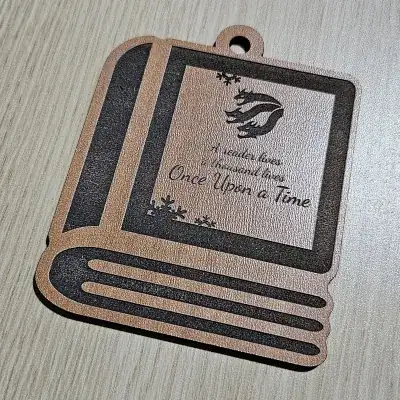 Book-shaped bookish ornament cut from cherry plywood, engraved with a dragon and the text A reader lives a thousand lives, Once Upon a Time