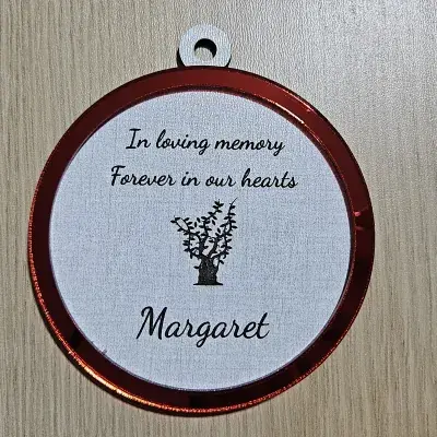 Round memorial ornament with a red mirror acrylic ring on linen plywood, engraved with In loving memory, Forever in our hearts, and the name Margaret above a tree