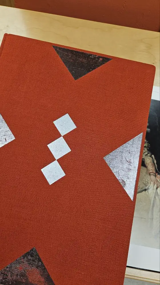 A rust red cloth bound book with silver geometric ornament on its cover