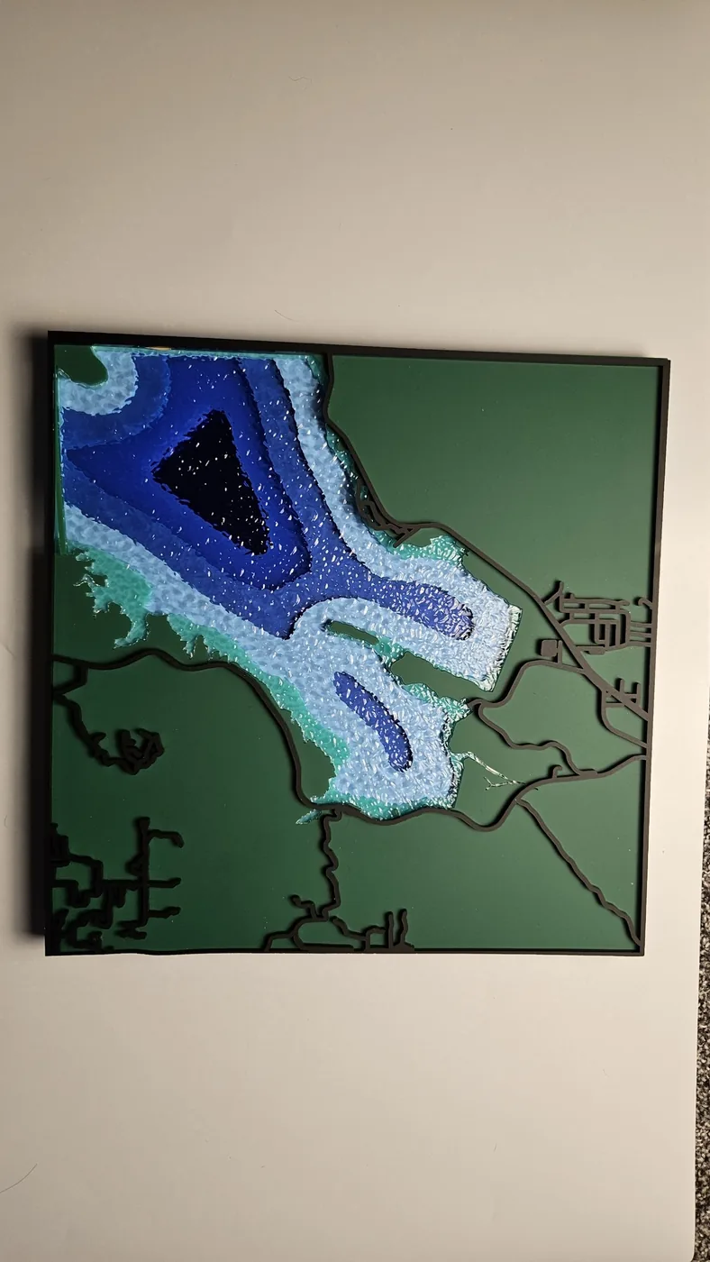 A laser-cut depth chart of an inlet with layered blue water bands on a green panel