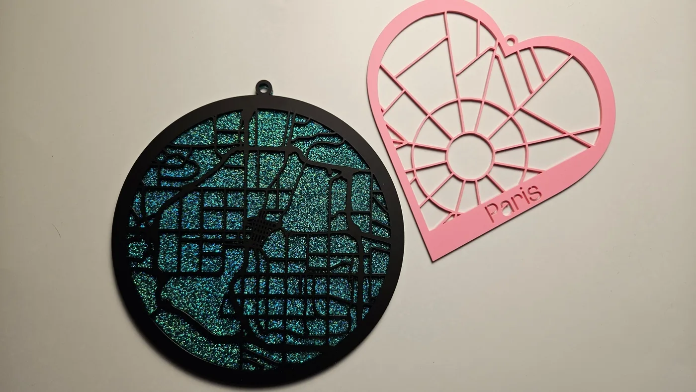 A round city map ornament in glitter acrylic beside a pink heart-shaped Paris map