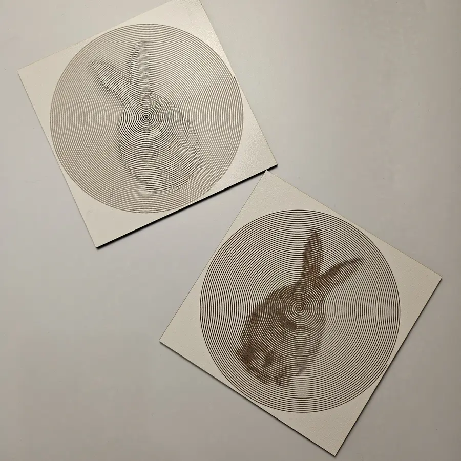 Two laser-engraved photo spirals of rabbits on white plywood
